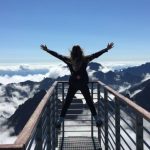 Unconventional Success - Person Standing on Hand Rails With Arms Wide Open Facing the Mountains and Clouds