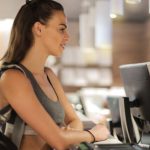 Athlete Business - Fit smiling sportswoman waiting at gym reception desk