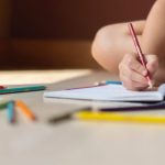 Skills Development - Crop kid sitting on floor and writing in notebook