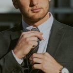 Thought Leader - Serious confident male entrepreneur wearing classy suit and wristwatch holding tie while thoughtfully looking away