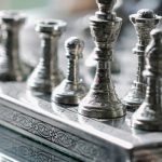 Competitive Strategy - Classic metal chess board with set figurines designed with carved ornaments and placed on glass table in light room