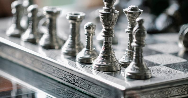 Competitive Strategy - Classic metal chess board with set figurines designed with carved ornaments and placed on glass table in light room