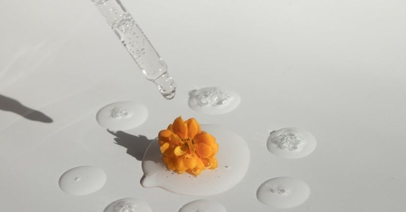 Wellness Productivity - From above of drops of transparent moisturizing cosmetic product dripped by pipette and small fresh flower head placed on white table