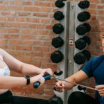 Exercise Benefits - Multiethnic trainer and overweight woman doing exercises with rowing machine together in sport club