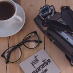 Covid Innovation - From above of coffee cup and eyeglasses placed on wooden table near folded drone and sticky note with post quarantine plan inscription