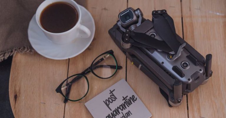 Covid Innovation - From above of coffee cup and eyeglasses placed on wooden table near folded drone and sticky note with post quarantine plan inscription